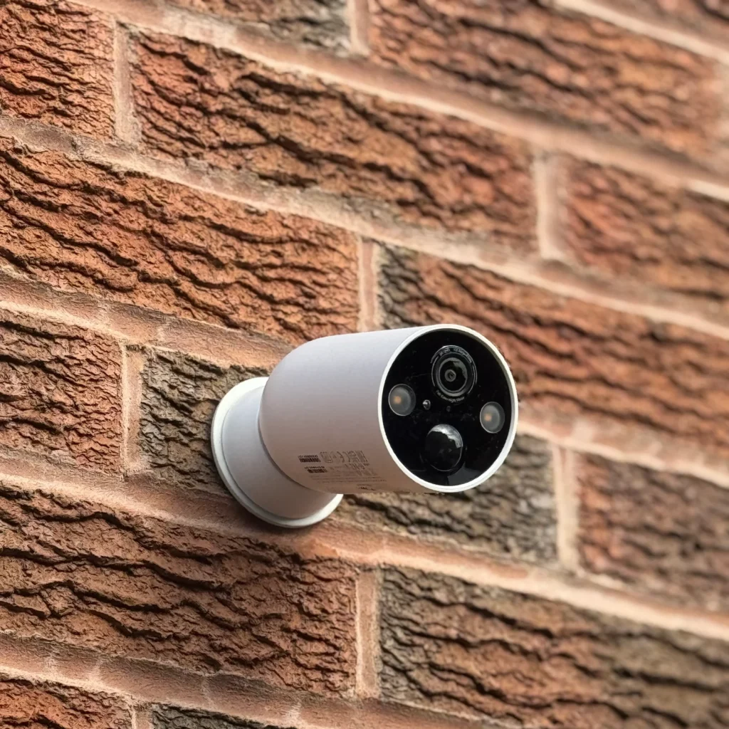 A white wireless security camera mounted on a brick wall outside a home.