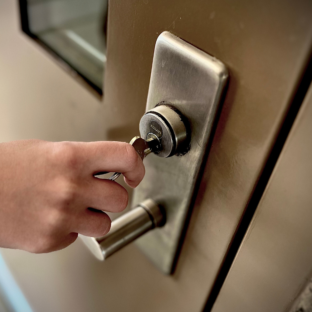 A hand turning a key in a sturdy commercial door lock on a metal door.